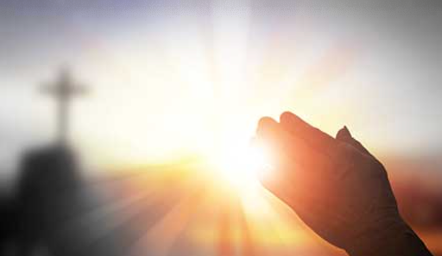 Hands folded in prayer with a cross in the background at Maryville Retreat Center during the spiritual healing retreat ‘Time for Healing.'
